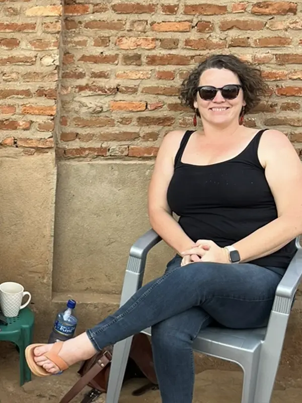 Nikki Eggers sitting in a gray chair in front of a brick wall, wearing a black tanktop and sunglasses