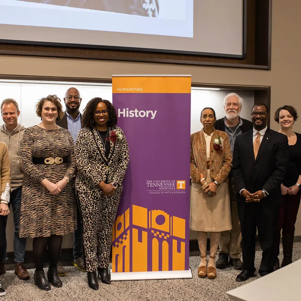 Faculty pose for a photo at an event by a UT History stand-up banner