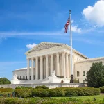 The Supreme Court buliding against a bue sky and green lawns.
